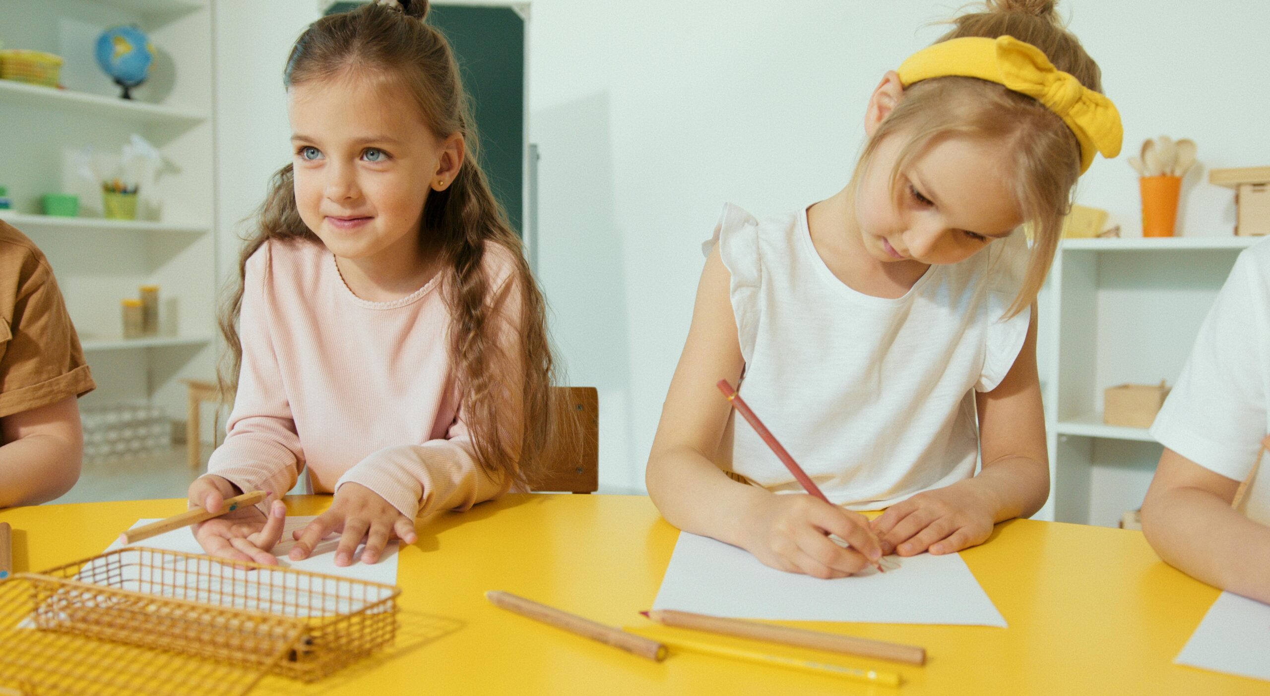 Home Two young girls writing and learning in a bright classroom setting.