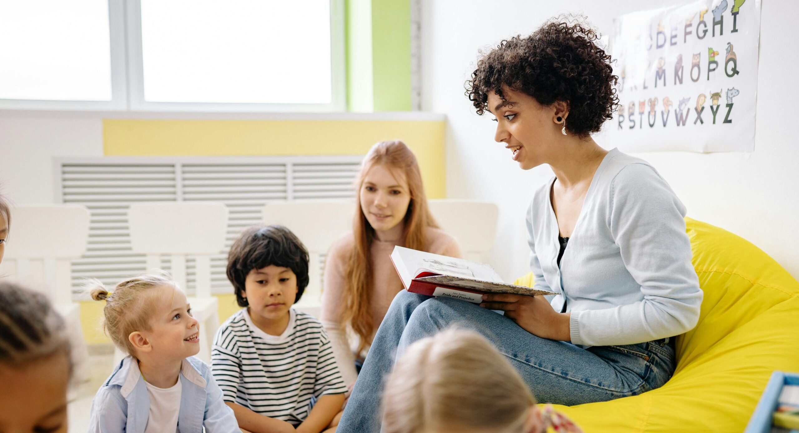 Home Teacher reading to preschool kids in a colorful classroom setting.
